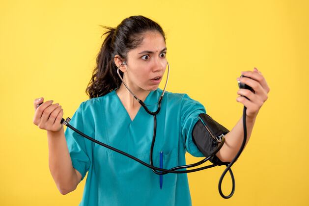 高尔夫前视图 穿着制服的女医生站在黄色背景上用血压计惊叹不已医疗器械使用背景