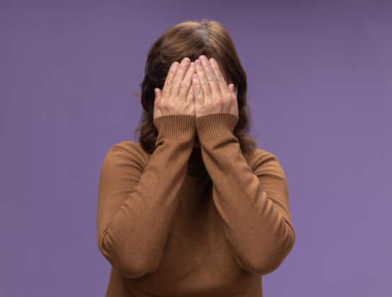 封闭中年妇女穿着棕色高领毛衣 闭着脸 胳膊站在紫色的墙上站着中间年龄