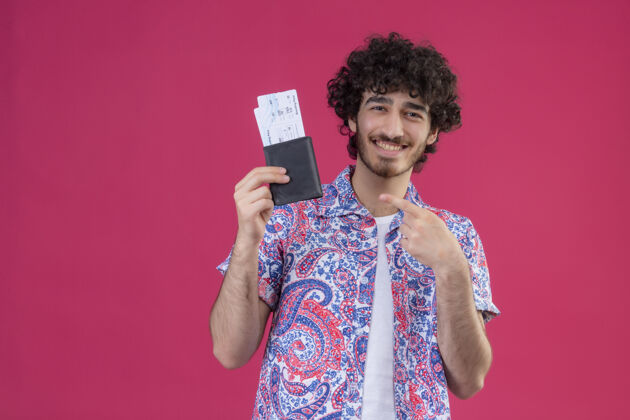 男人微笑着的年轻英俊的卷发旅行者 手里拿着钱包和机票 在有复印空间的粉色隔离墙上指着它们机票飞机帅哥