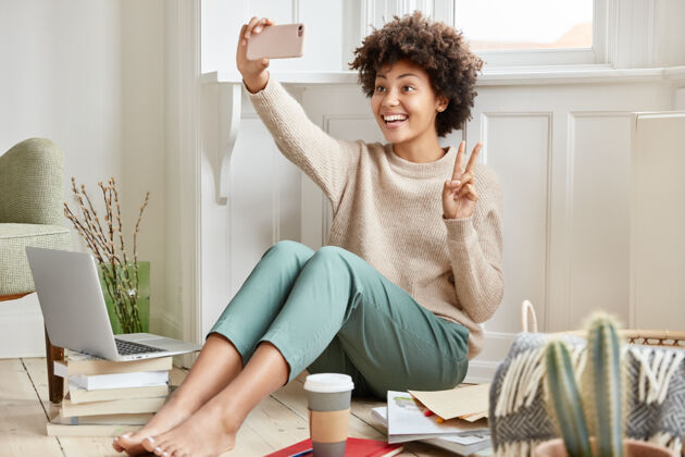 赤脚高兴的黑皮肤女性用手机打视频电话 显示和平迹象在线女士民族