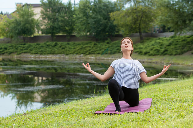 宁静年轻漂亮的女人在绿色公园做瑜伽练习健康的生活方式和健身理念手姿势早晨