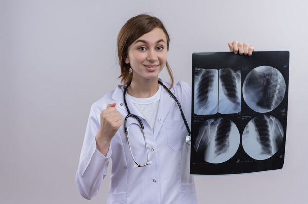 年轻年轻的女医生穿着医用长袍 戴着听诊器 拿着x光片 站在隔离的白墙上 留着复印空间X光长袍女