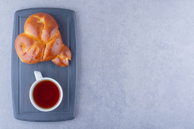 杯一杯茶和一个心形的甜面包放在大理石表面的海军蓝板上烘焙食品早餐美味