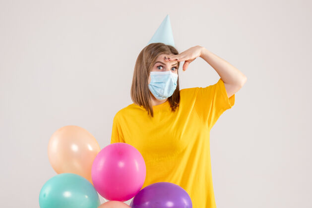 健康戴着白色面具手持彩色气球的年轻女性庆祝生日举行