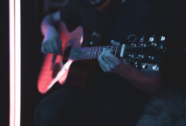 声学一个男人在黑暗的房间里弹原声吉他现场表演 原声音乐会手吉他手和弦