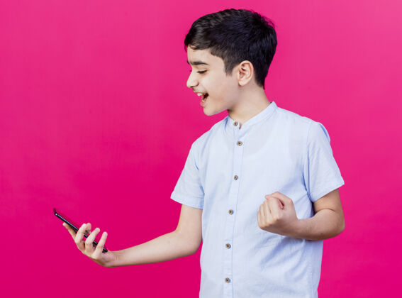 电话快乐的年轻白人男孩抱着看手机做是的手势孤立在深红色的背景是的快乐年轻