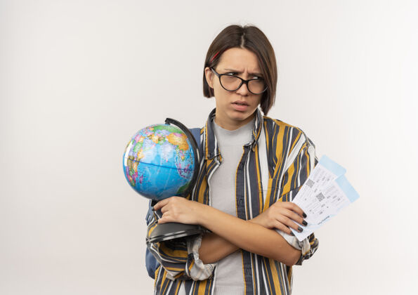 女孩恼怒的年轻女学生戴着眼镜 背着包拿着机票和地球仪 望着隔离在白色边上的复印空间飞机持有地球仪