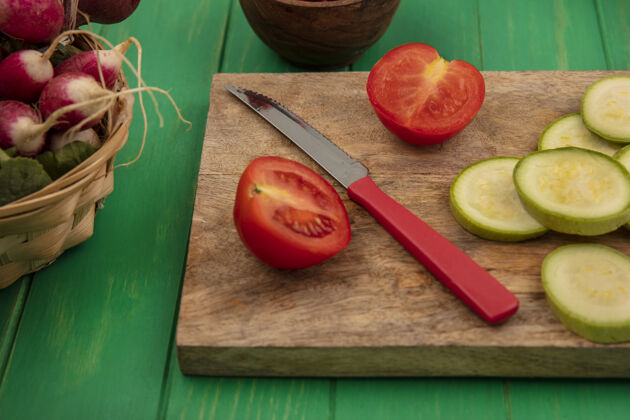 西红柿新鲜蔬菜的俯视图 比如西红柿和切碎的西葫芦片 它们被隔离在一个木制的厨房板上 在绿色的木墙上 用小刀和萝卜放在桶上顶部萝卜蔬菜