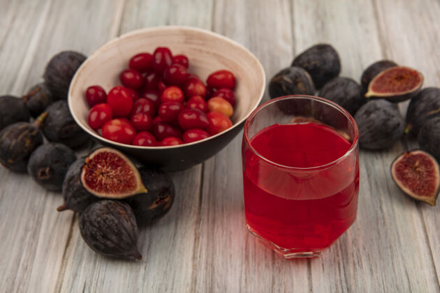 任务黑色使命无花果的顶视图 在一个碗上放着科尼利亚樱桃 在灰色的木墙上放着一个玻璃杯 上面放着新鲜的果汁水果新鲜樱桃