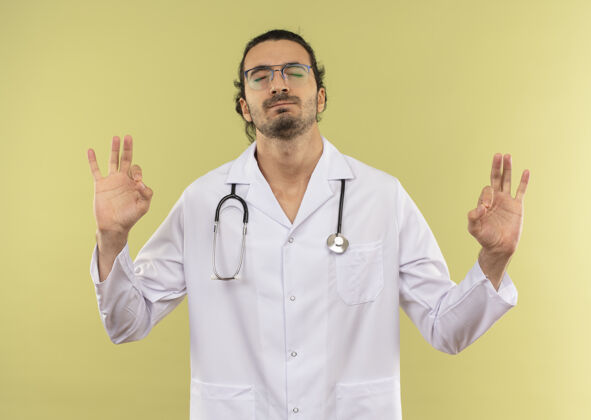 绿色年轻的男医生 戴着眼镜 身穿白色长袍 手持听诊器 眼睛紧闭 在绿色屏幕上显示出良好的手势长袍关闭眼睛