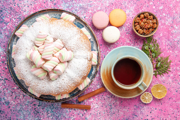 茶碟粉红色表面上有一杯茶和法式马卡龙的糖粉蛋糕俯视图茶麦卡龙马克杯