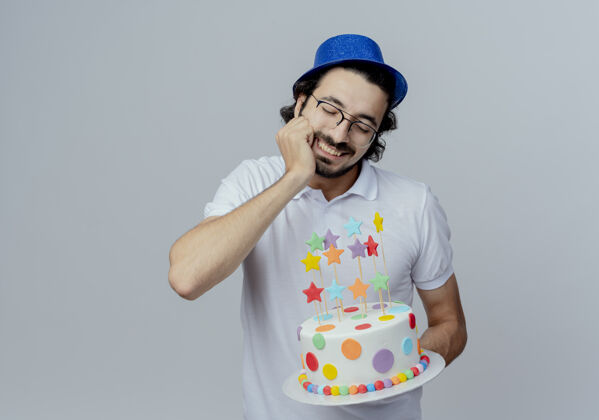 男人面带微笑的帅哥戴着眼镜 戴着蓝帽子 手里拿着蛋糕 手放在下巴下 隔着白色的头发帽子蛋糕眼镜