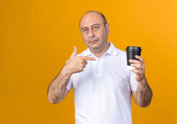 点随便成熟的男人拿着咖啡杯指着隔离在黄色墙上成熟孤立随意