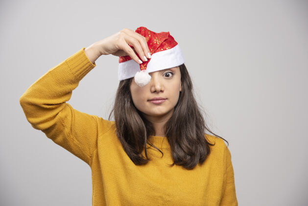 礼品盒戴着圣诞老人红帽子的年轻女子在白墙上摆姿势年轻女性帽子