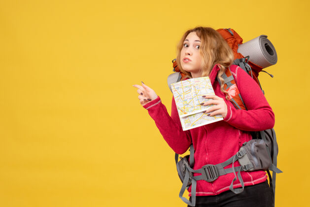 孩子俯视图：年轻迷茫的旅行女孩戴着医用面罩 拿着指向后面的地图 正在收拾行李人顶指向
