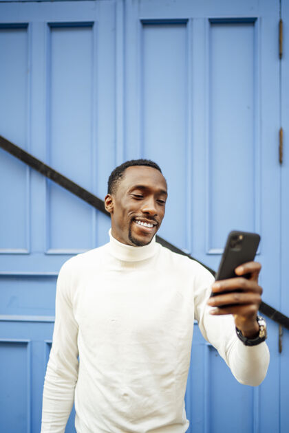 年轻一个穿高领毛衣的黑人看手机的垂直镜头垂直成人肖像