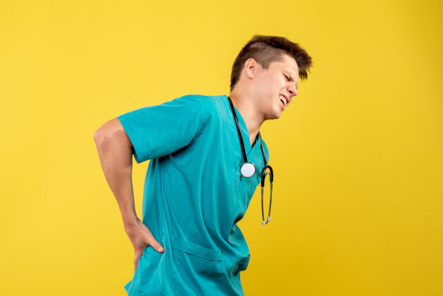男性黄墙上背疼的男医生 穿着医疗服 带听诊器医院疼痛前部