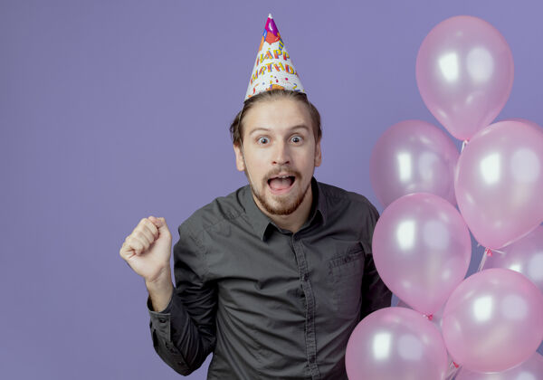 帽子一个戴着生日帽的帅哥拿着氦气球 在紫色的墙上把拳头孤立起来帅气拳头男人
