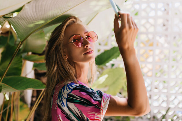 成人可爱的高加索女孩戴着粉色太阳镜抚摸着绿色的植物活跃女性背景