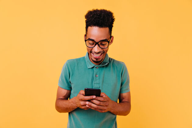 男孩戴着大眼镜的英俊黑人在看电话留言拿着智能手机的高兴的非洲男人的肖像卷发快乐非洲