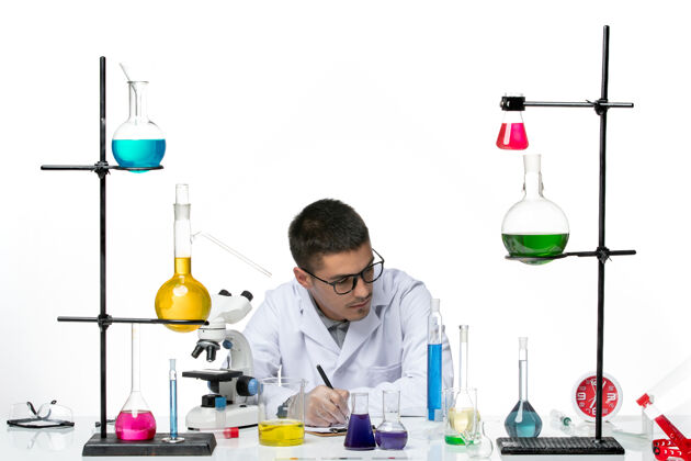 化学品正面图身着医疗服的男性化学家坐在白色背景上写笔记病毒冠状病毒飞溅疾病科学罐子科学实验
