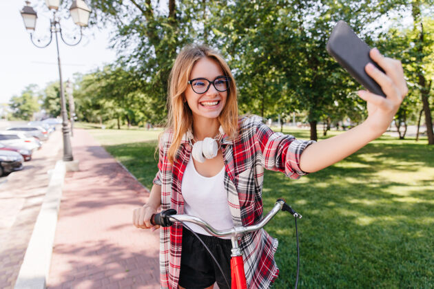 乡村热情有趣的女孩在公园里自拍漂亮的金发女模特骑着自行车拍照骑自行车耳机欧洲人