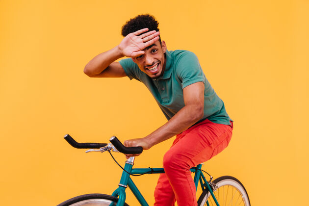 夏天笑脸男子卷发坐在自行车上非洲男子在五颜六色的服装骑自行车男人休闲活动