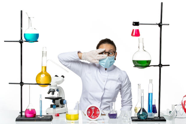 化学前视图：穿着医疗服的女化学家戴着面罩坐在白色地板上拿着溶液化学病毒实验室病毒-飞溅实验室医学视图