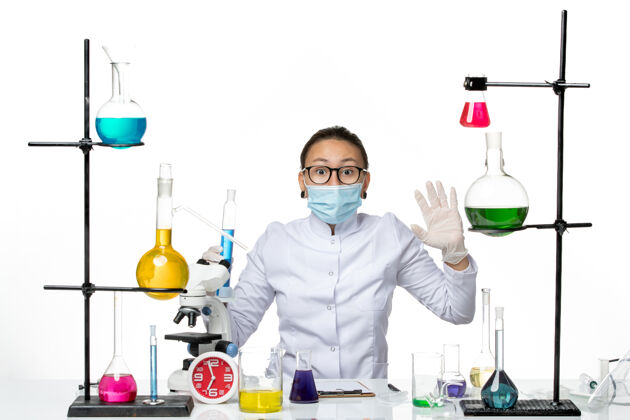 医学前视图：穿着医疗服的女化学家 戴着面罩 拿着白色背景上蓝色溶液的烧瓶 病毒化学实验室的covidsplash视图喷溅医学