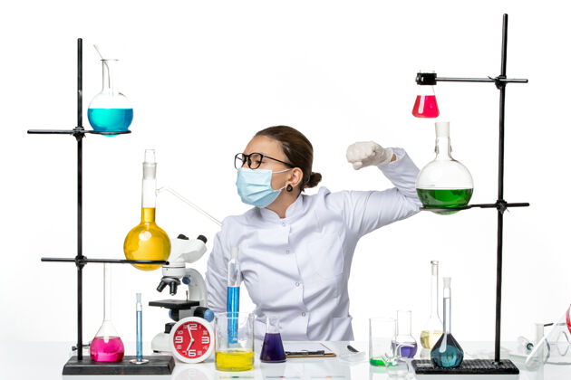 医疗前视图穿着医疗服的女化学家带着面罩坐在桌子前面 白色背景上有解决方案病毒化学实验室的covid飞溅物桌子医生坐