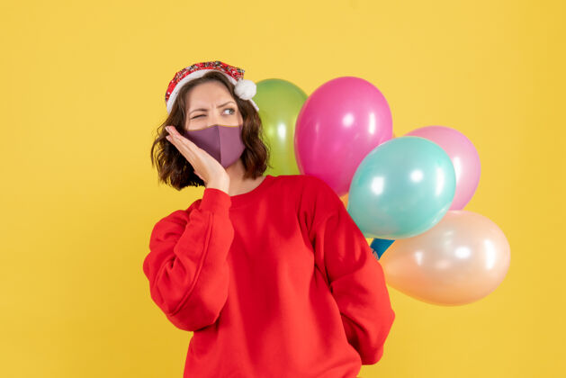 节日正面图年轻女性隐藏在无菌面具彩色节日情感新年圣诞气球面具消毒聚会