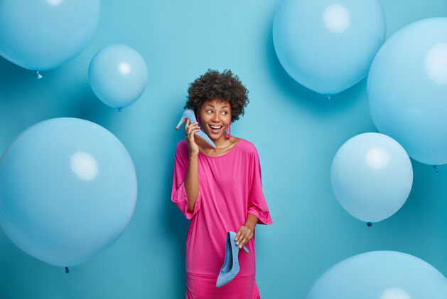 决定人和服装概念穿着粉色花式连衣裙 穿着高跟鞋 模仿电话 为派对穿衣服 展示她现代的衣橱蓝色的墙充气选择请