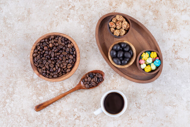 在咖啡豆和一杯煮好的咖啡旁边的一个木制托盘里放各种小吃釉面零食杯子