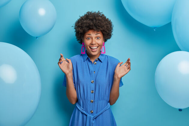 满意快乐的非洲裔美国妇女高兴地在聚会上遇到朋友 站在那里举手微笑 庆祝生日 穿着蓝色的裙子 迫不及待地打开礼物 身边有许多气球女人请微笑