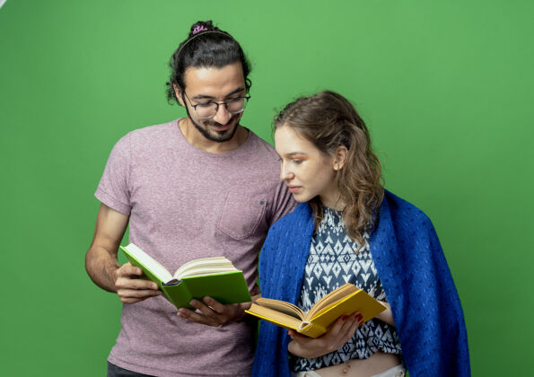 夫妻一对年轻夫妇拿着毛毯 手里拿着打开的书 快乐而积极地站在绿色的背景上年轻站着开放
