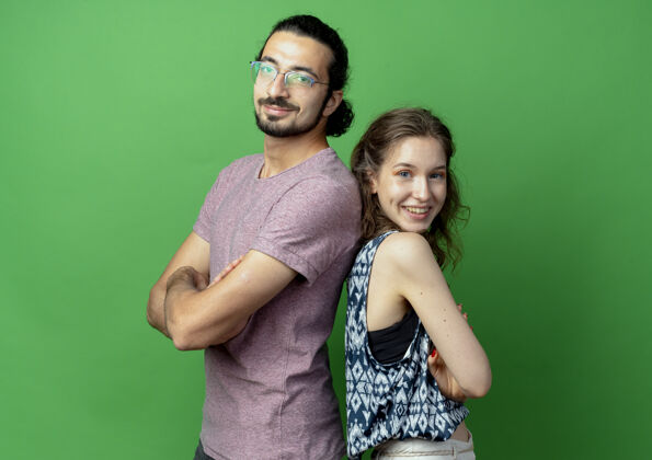 情侣一对年轻夫妇微笑着看着相机 背靠背地站在绿色背景上微笑镜头背