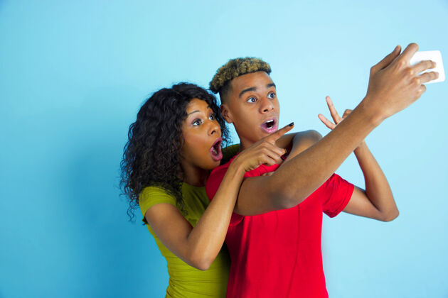 美国一起自拍或视频录影带年轻情绪化的非洲裔男女 穿着蓝色背景的彩色衣服美丽的情侣人类情感的概念 面部表情 关系 广告休闲化妆品姿势