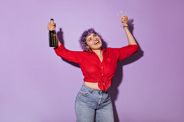 女人穿着衬衫和牛仔裤的紫色头发的迷人女人手里拿着玻璃杯笑着穿着鲜艳衣服的漂亮女人手里拿着一瓶酒女性学习夹克
