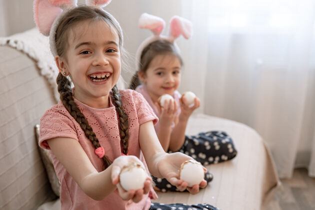 传统小妹妹们带着兔子耳朵和复活节彩蛋在家里的沙发上对着镜头摆姿势鸡蛋孩子房子