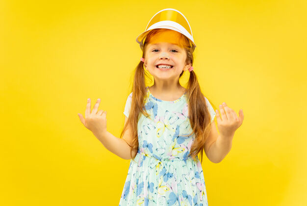 积极美丽动情的小女孩被隔离在黄色背景下半长的快乐和庆祝的画像 孩子穿着裙子和橙色帽子夏天的概念 人类的情感 童年衣服面部童年