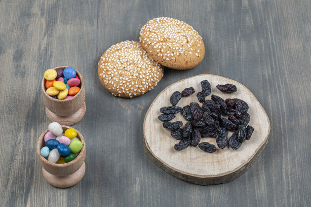 木板干葡萄干和面包和五颜六色的糖果放在木桌上葡萄干干的面包