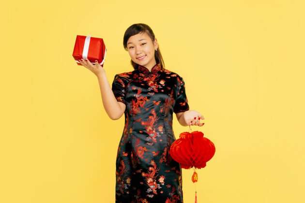 情感带着灯笼和礼物摆姿势 微笑着2020年中国新年快乐黄色背景上的亚洲少女肖像穿着传统服装的女模特看起来很快乐庆祝 情感复制空间中国愿望照明