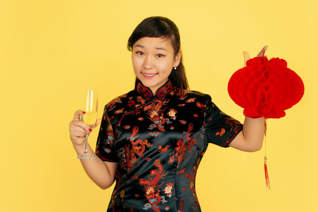 照明手持香槟和灯笼2020年中国新年快乐黄色背景上的亚洲少女肖像身着传统服装的女模特看起来很快乐庆祝 情感复制空间女孩微笑青少年