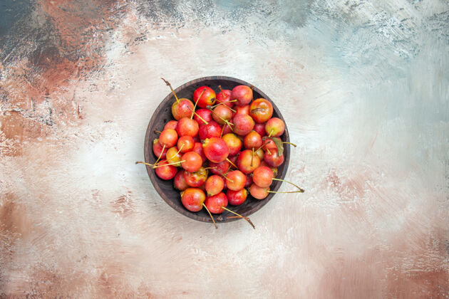 棕色樱桃的俯视图粉色-白色-灰色桌子上一碗红黄色的樱桃食物配料胡椒