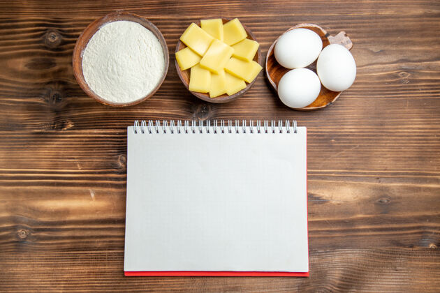 糕点俯视整个生鸡蛋与面粉记事本和奶酪在棕色的桌子上鸡蛋面团面团面粉粉粉粉顶部灰尘鸡蛋