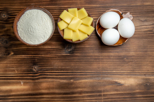 原料俯视整个生鸡蛋与面粉和奶酪在棕色的桌子上鸡蛋面团面粉粉尘产品鸡蛋面粉产品