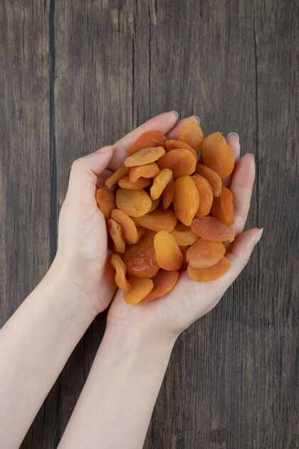 杏女人的手拿着一堆健康的杏干放在木桌上水果橘子美味