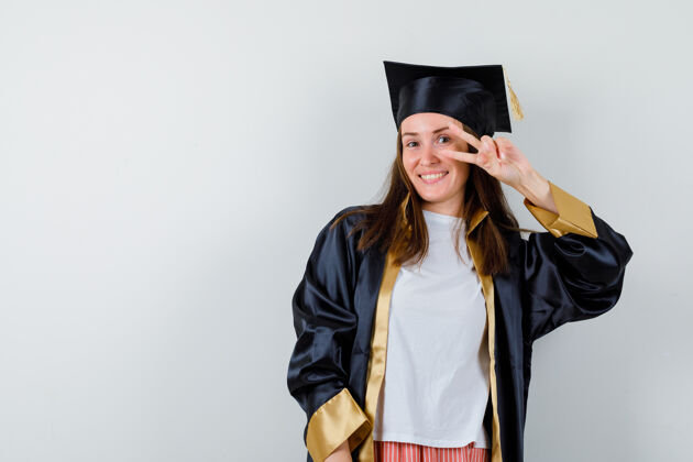 近女毕业生穿着学院服 眼睛附近有v字标志 看上去很快乐 正面照表演年轻学士