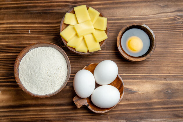 有机俯视整个生鸡蛋与面粉和奶酪在棕色的桌子上鸡蛋早餐面团面团面粉粉粉粉景观生的糕点