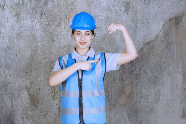 姿势女工程师戴着蓝色的头盔和装备 展示她的手臂肌肉工程师女人标准